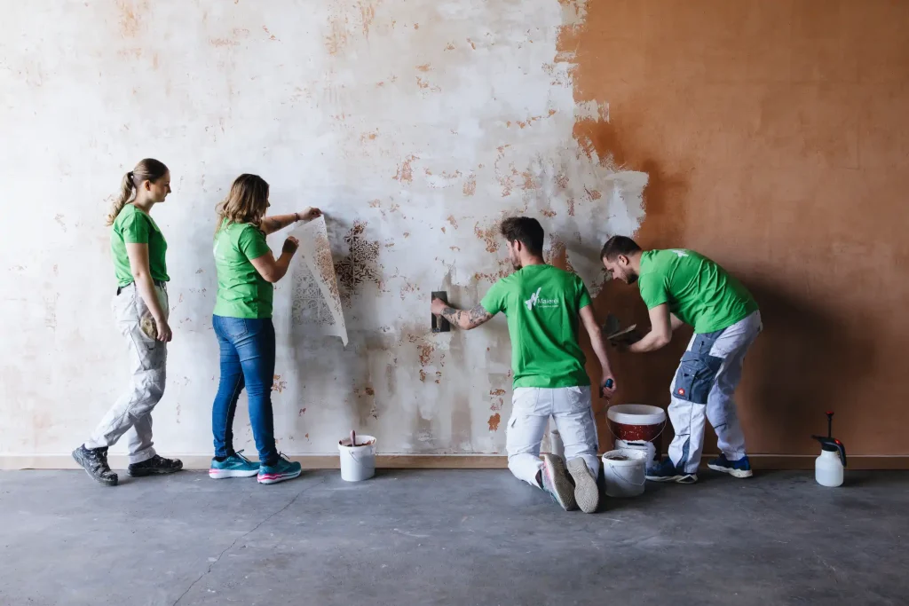 Zwei Frauen und zwei Männer beim Spachteln und Bemalen einer Wand